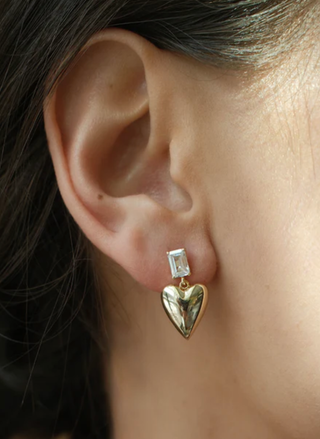 Gold heart-shaped earring with a clear gemstone worn by a person.