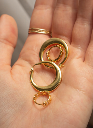 Gold hoop earrings held in a hand against a neutral background