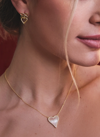 Close-up of a woman wearing gold heart-shaped earrings and necklace.