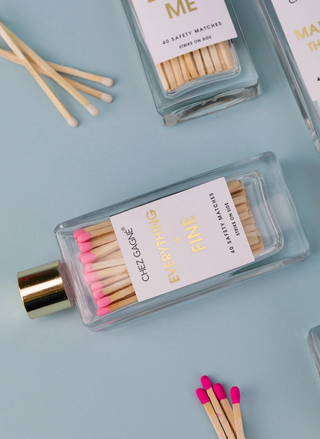 Glass bottle matches with gold lettering that reads Everything Is Fine laying down on a blue background.