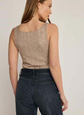 Woman wearing a beige sleeveless top and dark jeans against a plain background