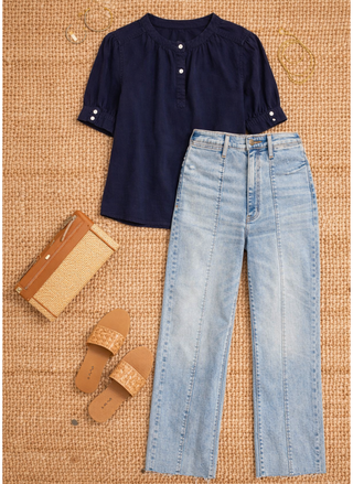 Navy blouse, light blue jeans, brown sandals, and a woven bag on a textured surface