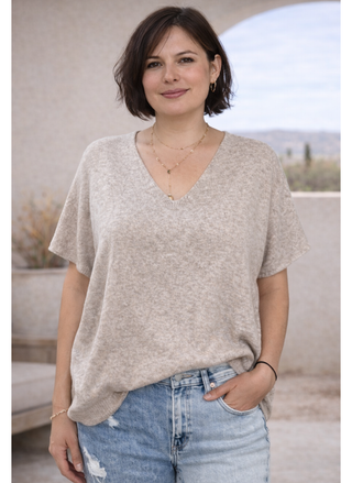 Woman wearing a beige v-neck sweater tee and blue jeans outdoors