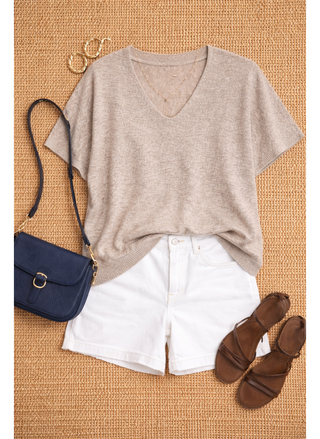 Beige top, white shorts, navy bag, and brown sandals on a textured surface