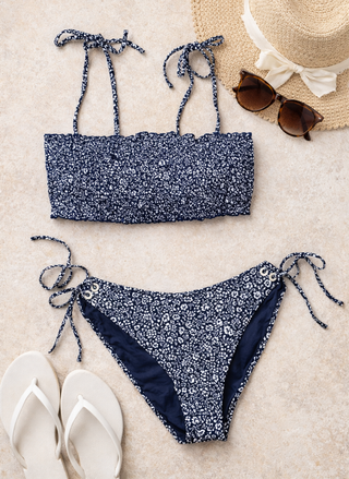 Navy floral bikini set with matching top and bottom on a sandy surface, accompanied by a hat, sunglasses, and flip-flops.