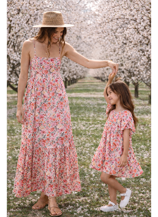 Woman and young girl in matching floral dresses standing in a cherry blossom garden.