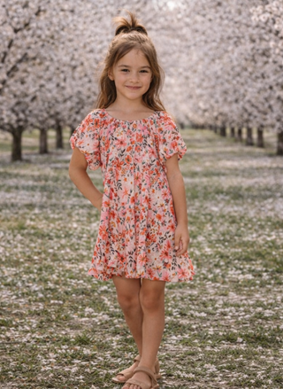 Young girl in a floral dress standing in a field of cherry blossom trees wearing Saltwater Luxe Maggie Dress.