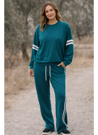 Woman wearing a teal tracksuit with white stripes standing outdoors.