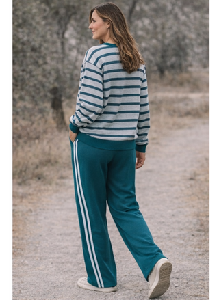 Woman wearing a striped sweater and teal tracksuit with white stripes walking on a gravel path.