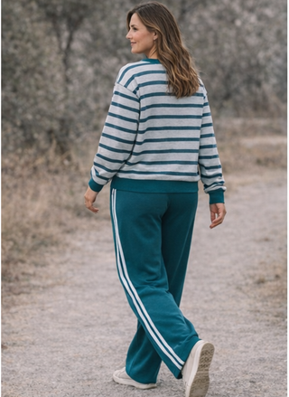 Woman wearing a striped sweater and teal tracksuit with white stripes walking on a path.