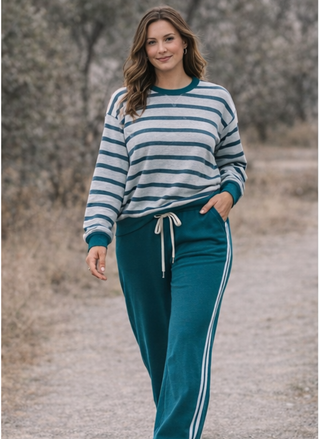 Woman wearing a striped sweater and teal pants with white stripes outdoors.