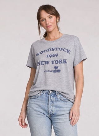 Woman wearing a gray t-shirt with 'Woodstock 1969 New York' text on a plain background.  Made by Chaser.  