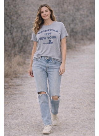 Woman wearing a 'Woodstock 1969 New York' t-shirt and ripped jeans on a gravel path.