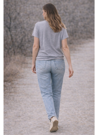 Woman walking away wearing a gray t-shirt and light blue jeans on a gravel path.