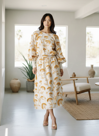 Woman wearing the Ciebon Wonda white and gold embroidered midi skirt with asymmetrical fringe detail in a neutral desert home setting.
