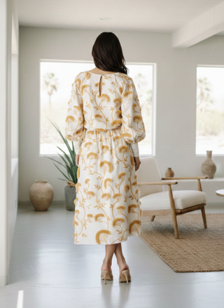 Back view of a woman wearing the Ciebon Wonda white and gold embroidered midi skirt with asymmetrical fringe detail in a neutral desert home setting.