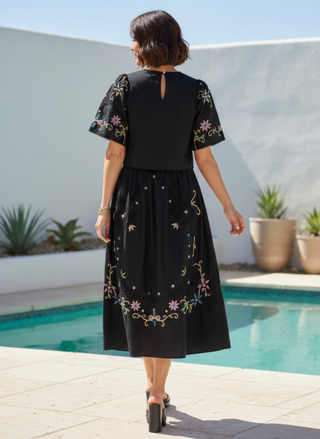 Back view of a woman wearing a black dress with floral embroidery by a poolside.