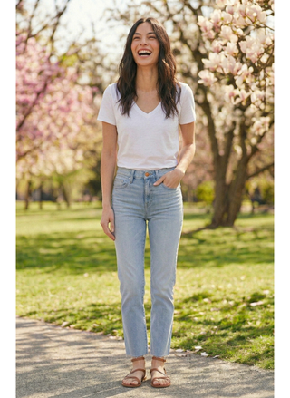 Woman in a white t-shirt and light indigo Porter Blue Rebel Straight Denim jeans standing in a park with cherry blossom trees.