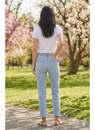 Person wearing a white t-shirt and light blue jeans standing in a park with cherry blossom trees.
