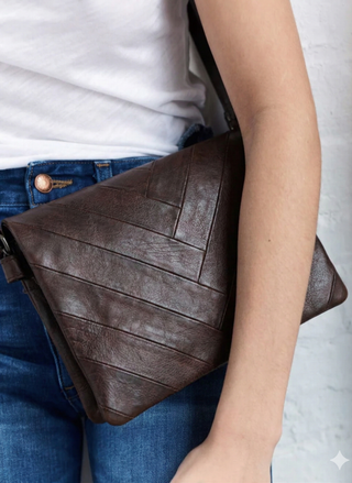 Brown leather bag held by a person wearing blue jeans and a white shirt.