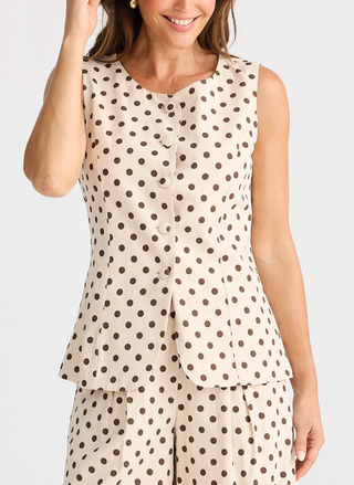 Woman wearing a beige sleeveless top with brown polka dots on a white background