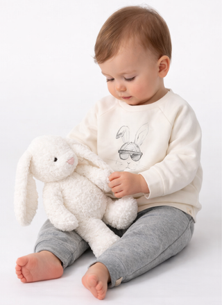 Child wearing Burt’s Bees Hip Hop Bunny baby sweat set with cream sweatshirt and gray jogger pants, sitting on a light gray background