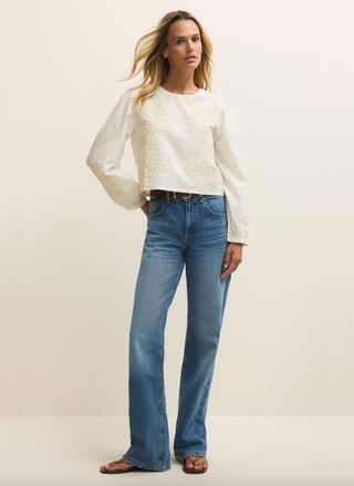 Woman wearing a white blouse and blue jeans against a plain background