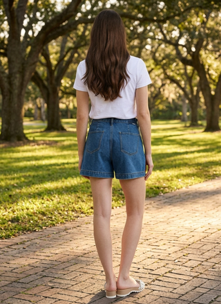 Person wearing a white t-shirt and blue denim shorts standing on a brick path in a park.