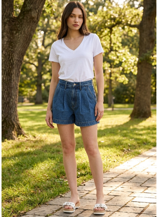 Woman wearing the DAZE Denim Coronado dark wash 100% cotton pleated high-rise shorts, standing on a sun-dappled park path.