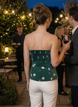Woman in a green strapless top with white polka dots and white pants standing outdoors at night.
