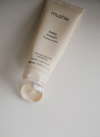 A close-up of the smooth, white Mushie Baby Cream being applied to a small area of skin, highlighting its rich texture.