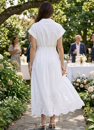 Woman in a white dress walking through a garden with people and tables in the background