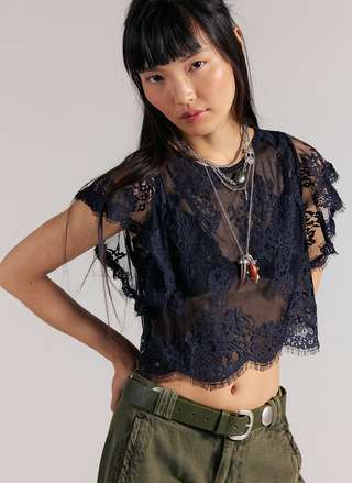 Woman wearing a dark lace top and green pants against a plain background