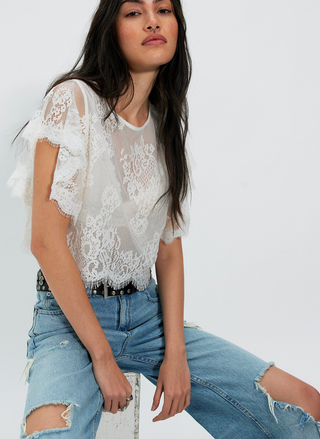Woman wearing a white lace top and blue jeans on a white background