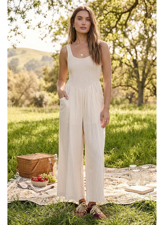 Model wearing Saltwater Luxe Leia Striped Jumper in sand and white stripes with a smocked bodice and wide legs at a park with a picnic in the back.