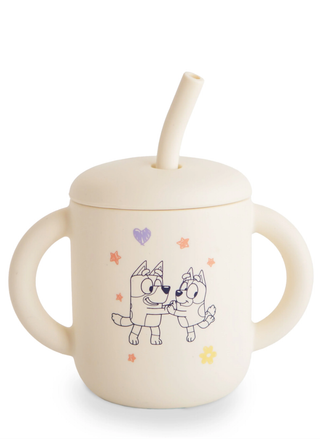 A cream-colored Mushie x Bluey silicone training cup with a matching straw and lid, featuring subtle Bluey and Bingo character illustrations.