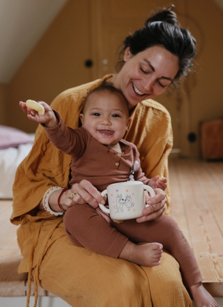 Woman holding a baby and a mug in a cozy indoor setting