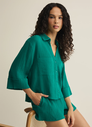 Woman wearing a green outfit sitting on a chair against a beige background