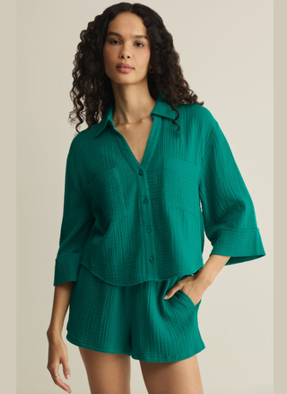 Woman wearing a green Z Supply Helena Cotton Gauze shirt and shorts set against a beige background