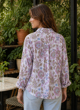Woman wearing a floral blouse standing outdoors with plants in the background