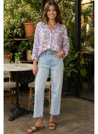 Woman wearing a floral blouse and light blue jeans standing outdoors.