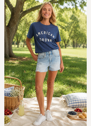 Front view of model wearing the blue Z Supply American Boyfriend Tee with "American Grown" graphic and light-wash denim shorts.