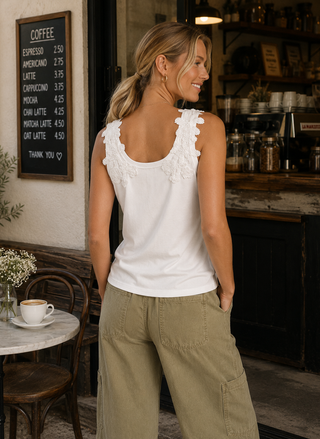Woman in a white sleeveless top and beige pants standing in a cafe.