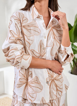 Person wearing a white shirt with brown floral patterns, standing indoors.