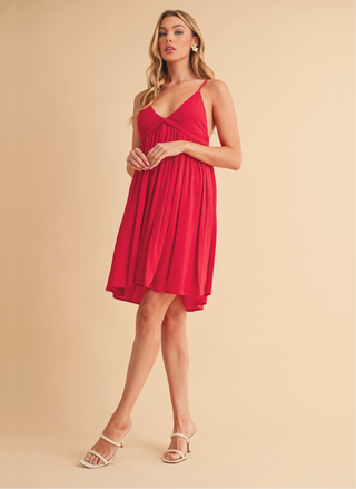 Woman wearing a short red strappy dress against a beige background