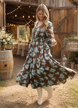 Woman in a floral dress standing in front of a rustic wooden building with string lights.