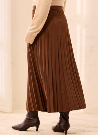 A brown pleated midi skirt worn with a cream sweater and dark brown pointed-toe ankle boots, shown from the waist down in a softly lit indoor setting.