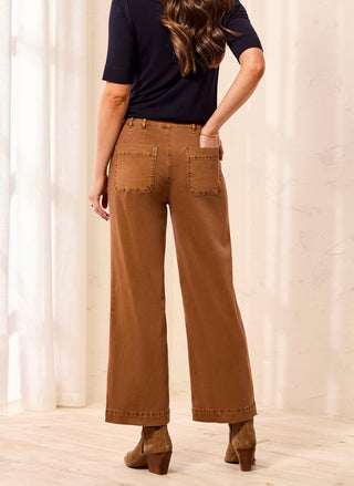 A woman shown from the back wearing brown wide-leg cropped pants, a dark navy short-sleeve top, and brown heeled ankle boots in a softly lit indoor setting with light curtains and a pale floor.