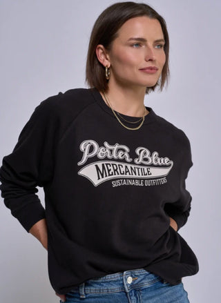 A woman wearing a black Porter Blue crewneck sweatshirt with a white graphic print that reads 'Porter Blue Mercantile Sustainable Outfitters' on the front, paired with blue jeans, against a plain light gray studio background.