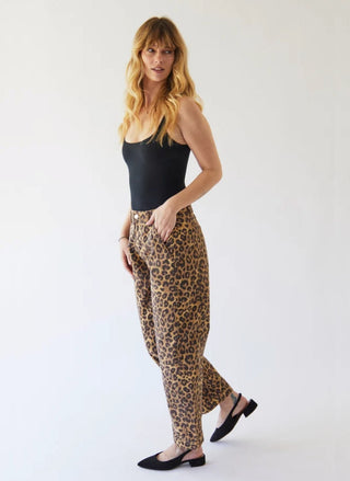 A woman modeling leopard-print pants, a black tank top, and black flat shoes against a plain white studio background.